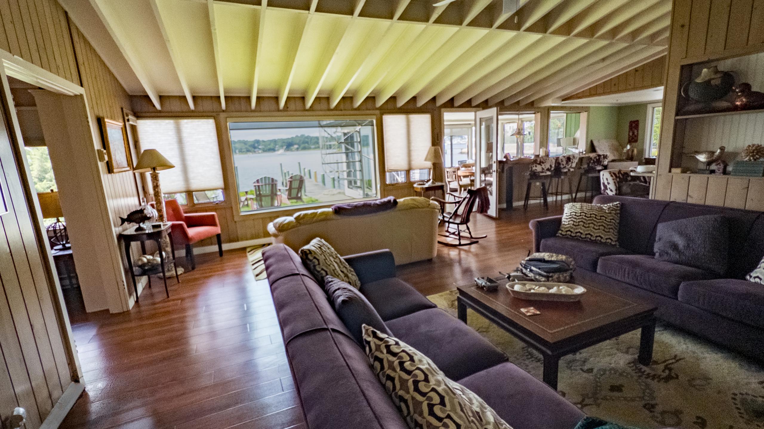 The living room: sectionals facing the picture window, with the dock and Adirondack chairs on the point just outside.