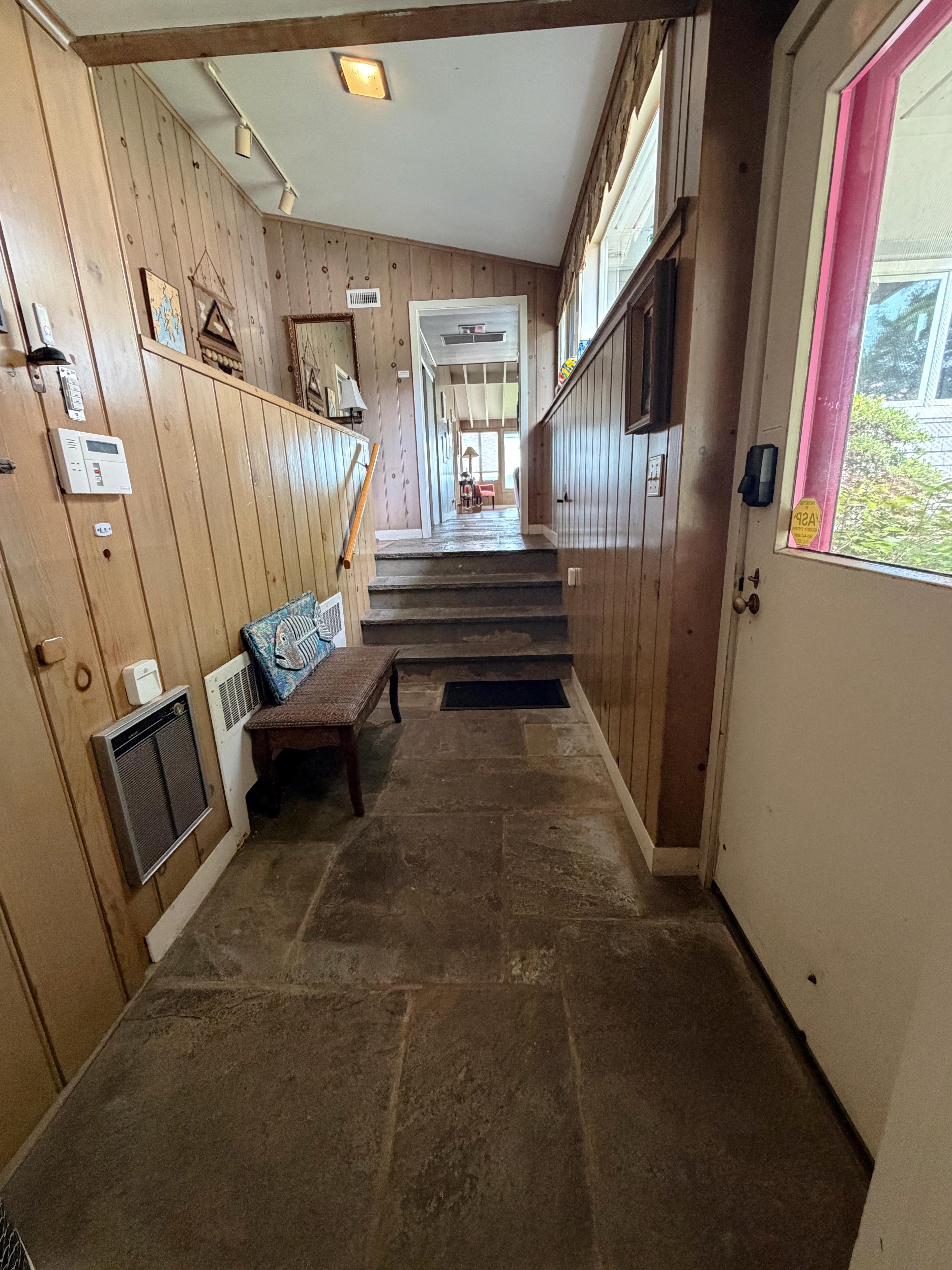 The flagstone entry hall: the purple screen door, a bench with a fish pillow, and the steps up to the main level with the sunroom beyond.
