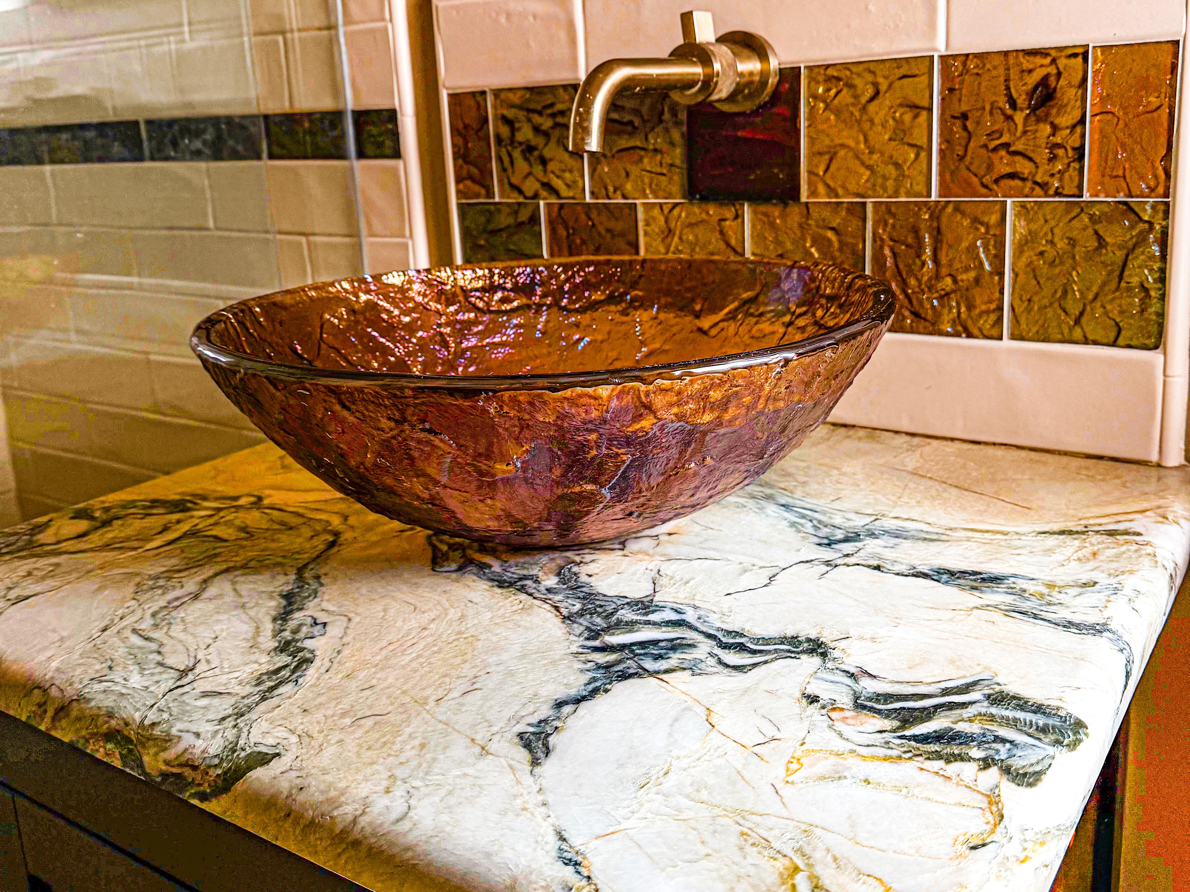 The downstairs bath's sink: an iridescent glass bowl on veined marble, filled from a wall-mounted bronze faucet.