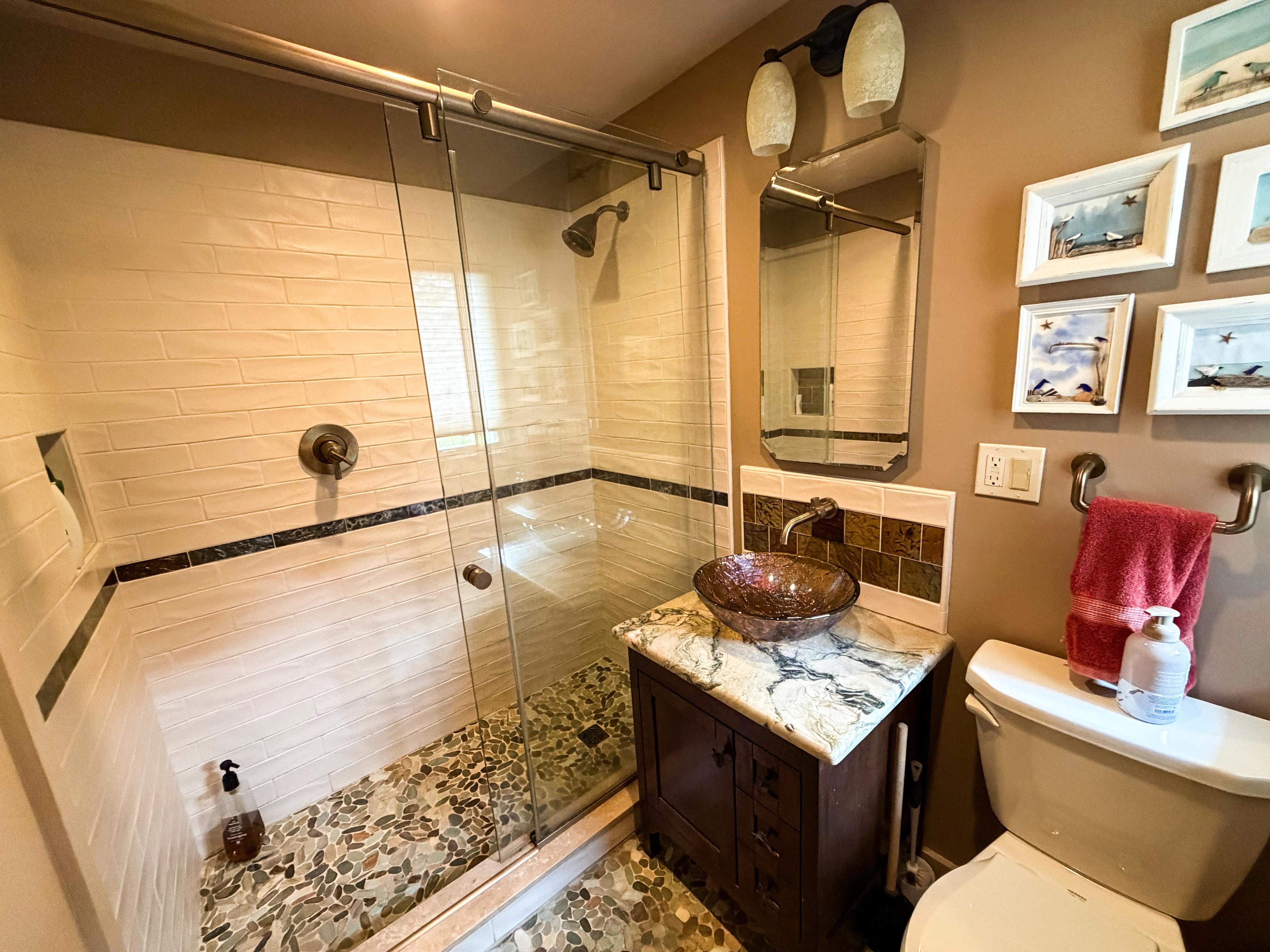 The downstairs bath: glass-door subway-tile shower with a pebble floor beside the dark-wood vanity.
