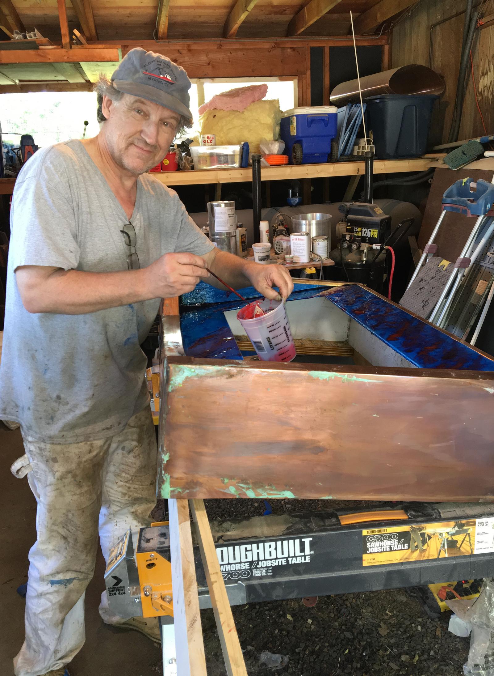 Chuck at work in the shop, brush in hand, painting patina onto a copper panel