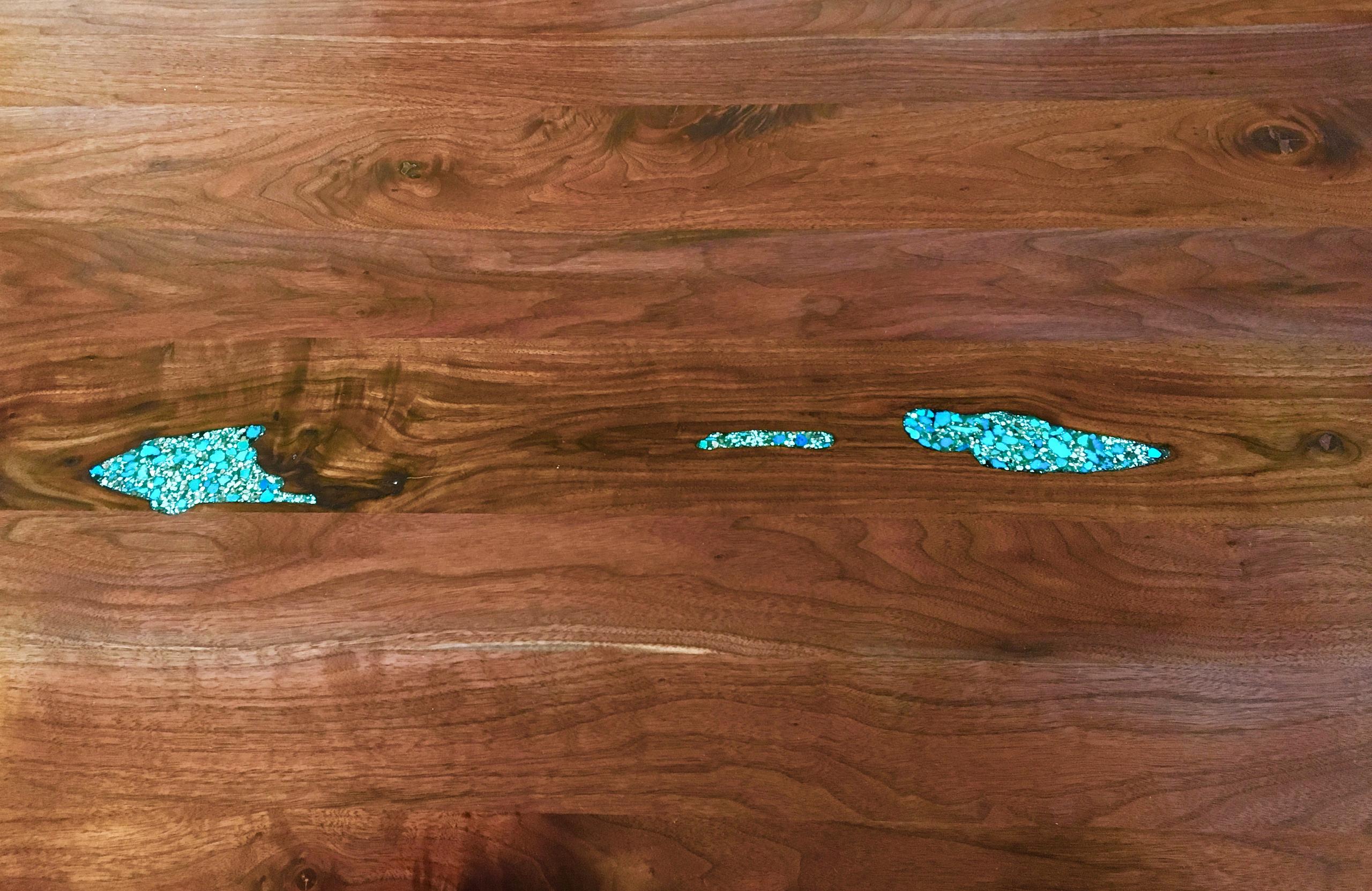 Overhead of the walnut island top: three natural voids in the grain filled with crushed turquoise chips.