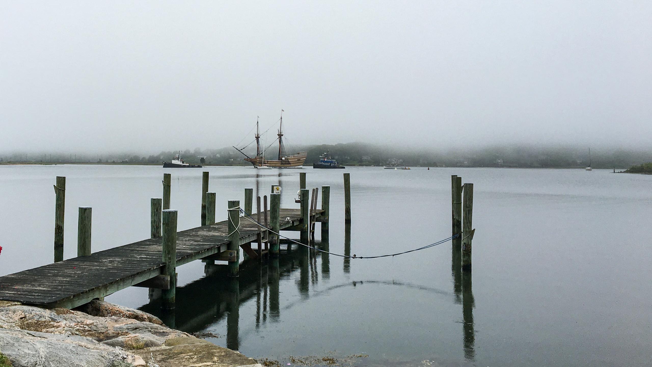 A tall ship at anchor off the point, appearing out of the morning fog.